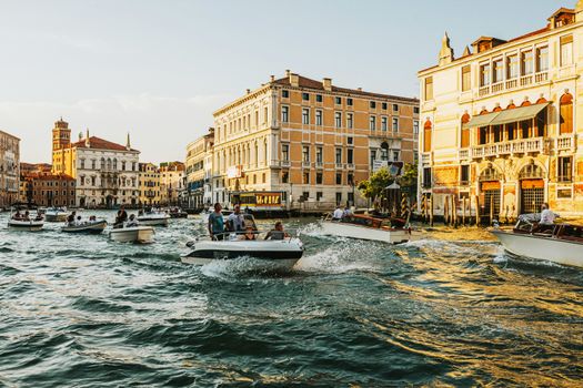 Lively scene of boats traversing the Grand Canal in Venice with historical buildings illuminated by sunset.