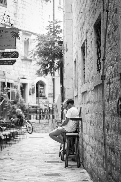 Men Sitting on Stools near Wall on Old Town Alley