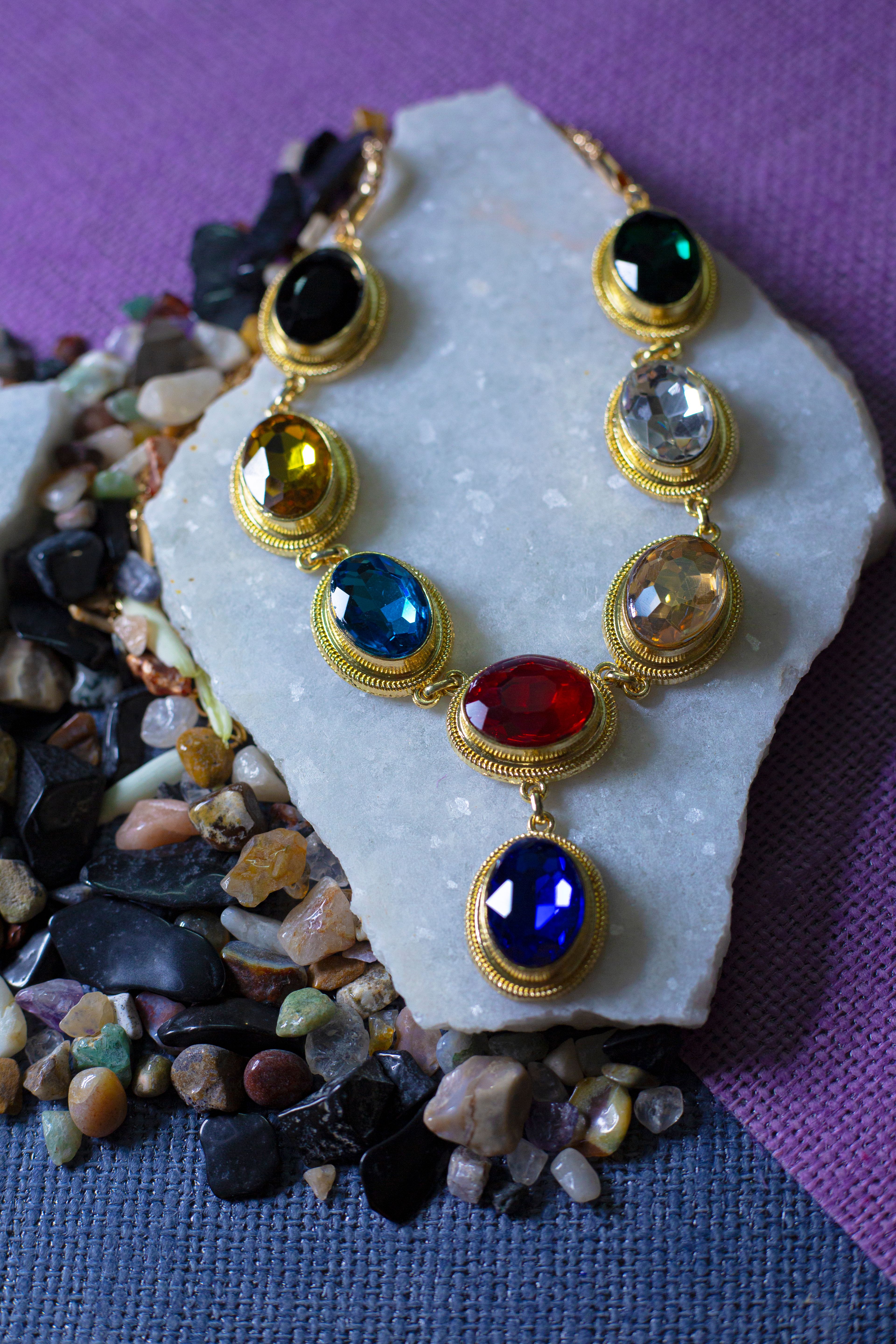 Vibrant necklace with multicolored gemstones including sapphire and emerald tones displayed on a white marble surface