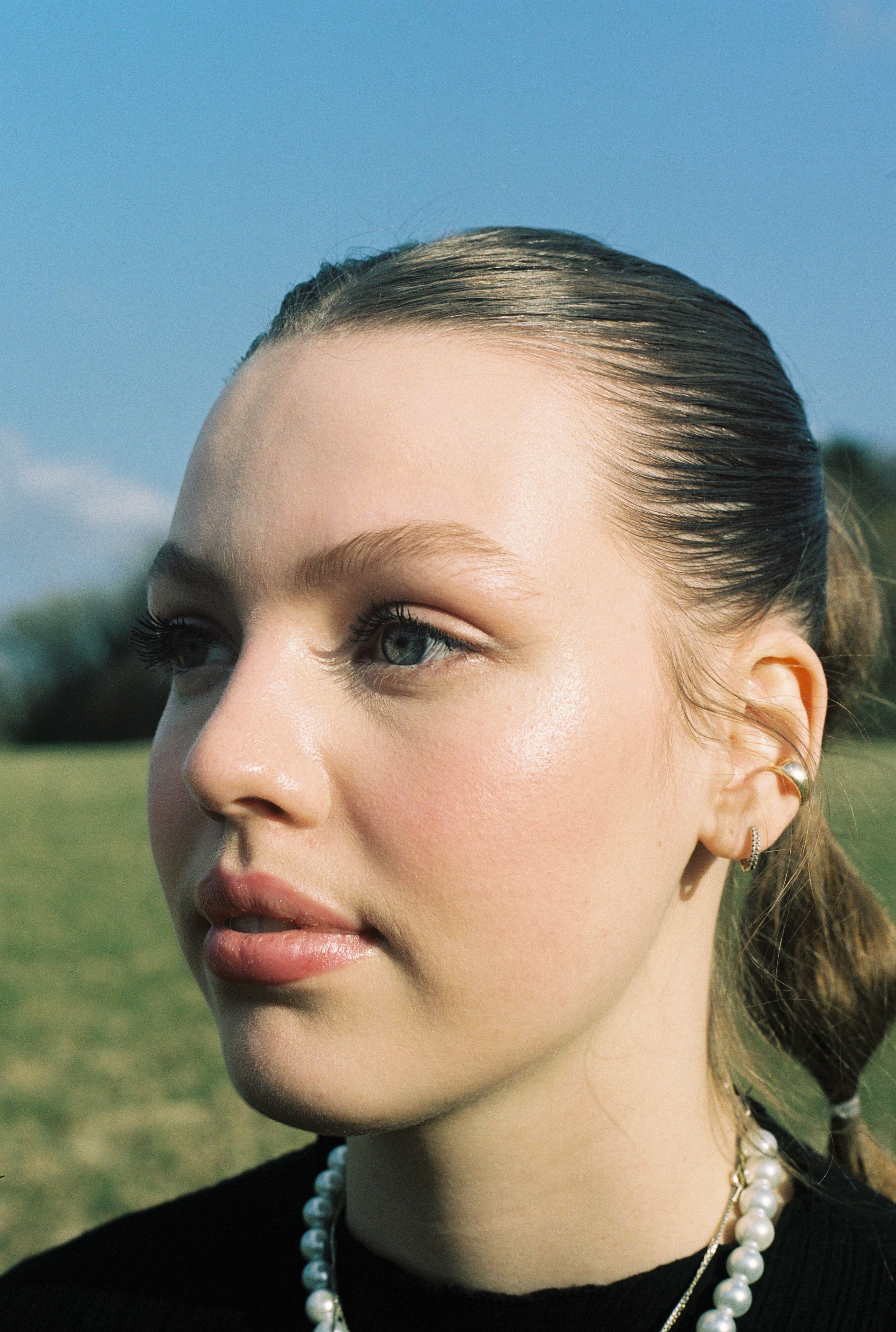 Close-up portrait of a woman with jewelry in a natural outdoor setting against a clear blue sky.