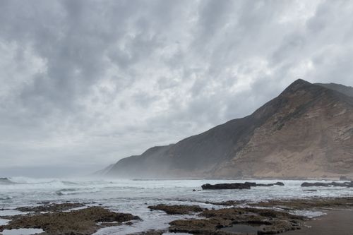 Free Dramatic coastal scene with foggy mountains and mist over the ocean waves. Stock Photo
