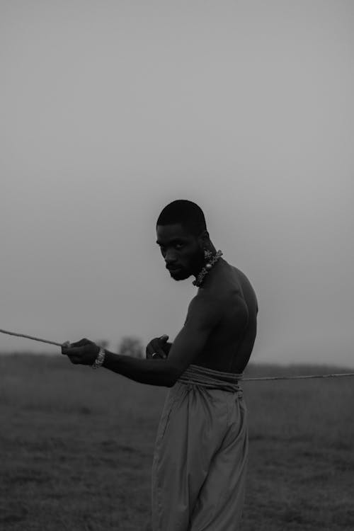 A Grayscale of a Shirtless Man Holding a Stick