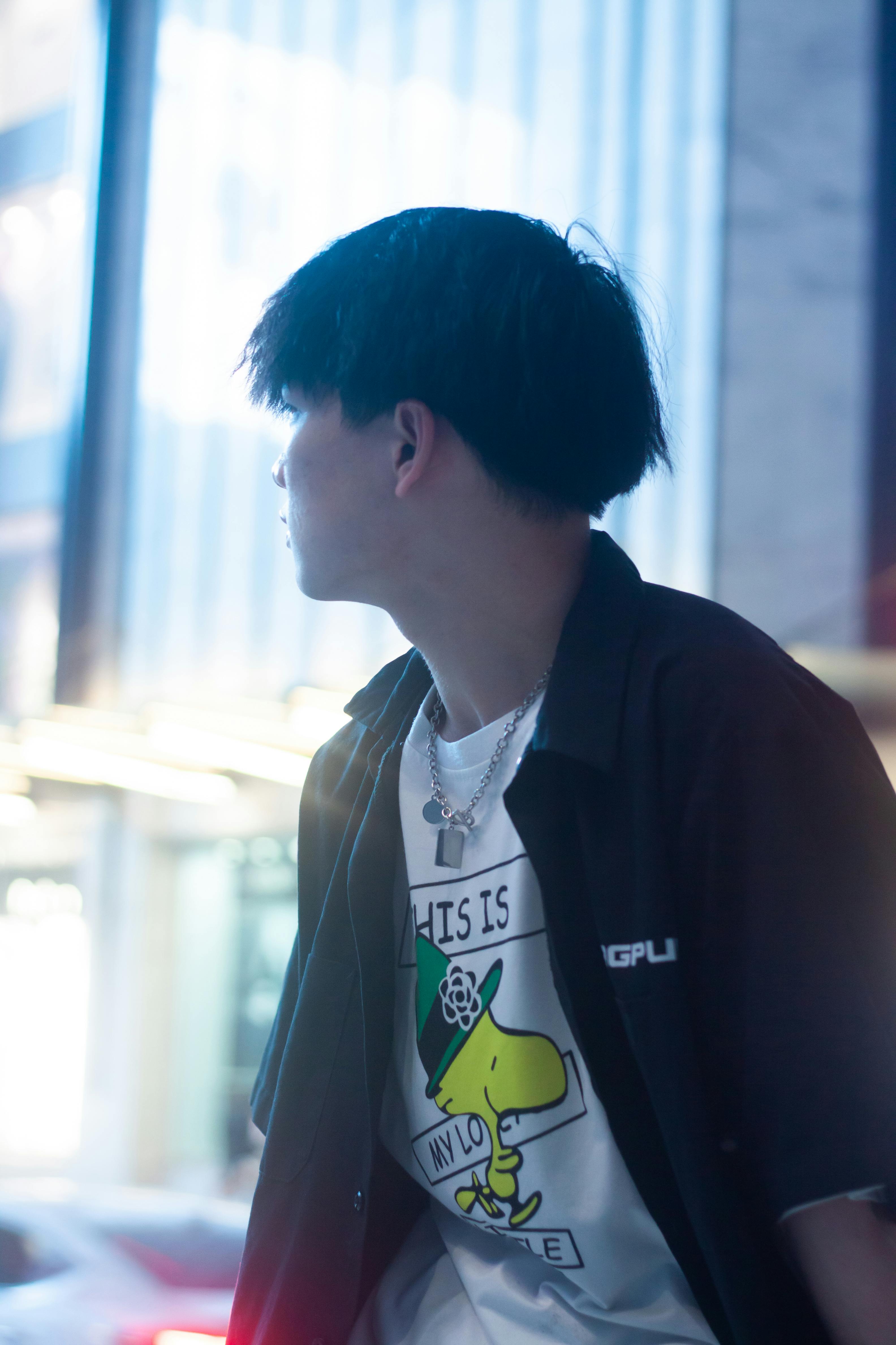 Young man in urban setting wearing a graphic tee and black jacket, looking away.