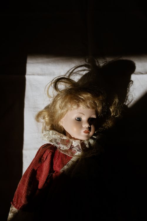 Free A vintage doll in a red dress lit by dramatic shadows, creating a spooky ambiance. Stock Photo