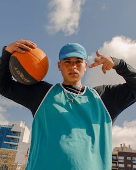 Portrait of a young man in sports attire holding a basketball outdoors against a cityscape backdrop.