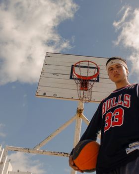 Portrait of a young basketball player holding a ball against a clear sky, ready for action.