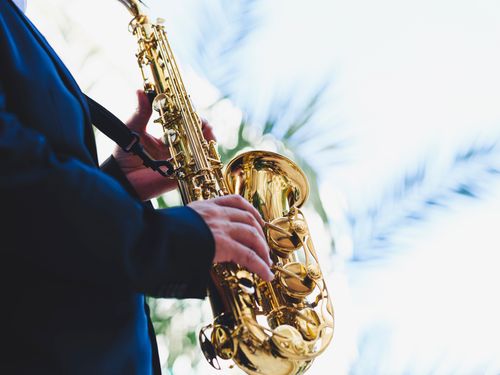 Free A musician in a suit plays a golden saxophone against a bright sky, showcasing musical talent and outdoor ambiance. Stock Photo