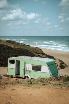 A retro camper parked on a coastal cliff with a breathtaking view of the beach and ocean.