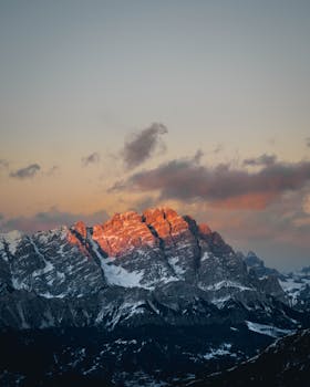 Breathtaking view of snow-covered mountains with a warm sunset glow and dramatic clouds.