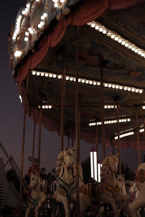 Free A beautifully lit carousel with horse figures shines brightly against the evening sky in a funfair setting. Stock Photo