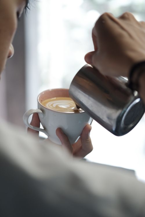 Free Close-up of a barista pouring latte art into a coffee cup, showcasing precision and skill. Stock Photo