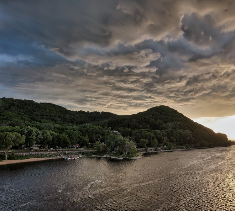 A Green Tree Filled Mountain Beside River Under Cloudy Sky