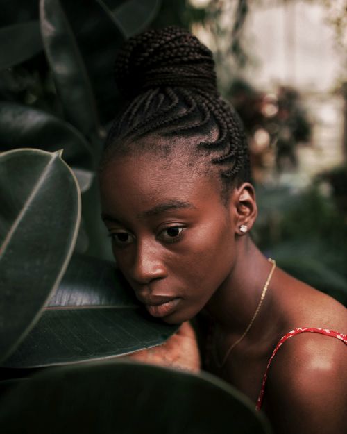 Free A contemplative woman with braided hair surrounded by vibrant, exotic plants in a botanic setting. Stock Photo