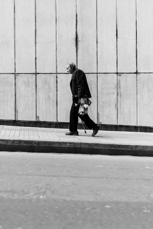 Free Man walking on Bogotá sidewalk in black suit against a textured wall, monochrome style. Stock Photo