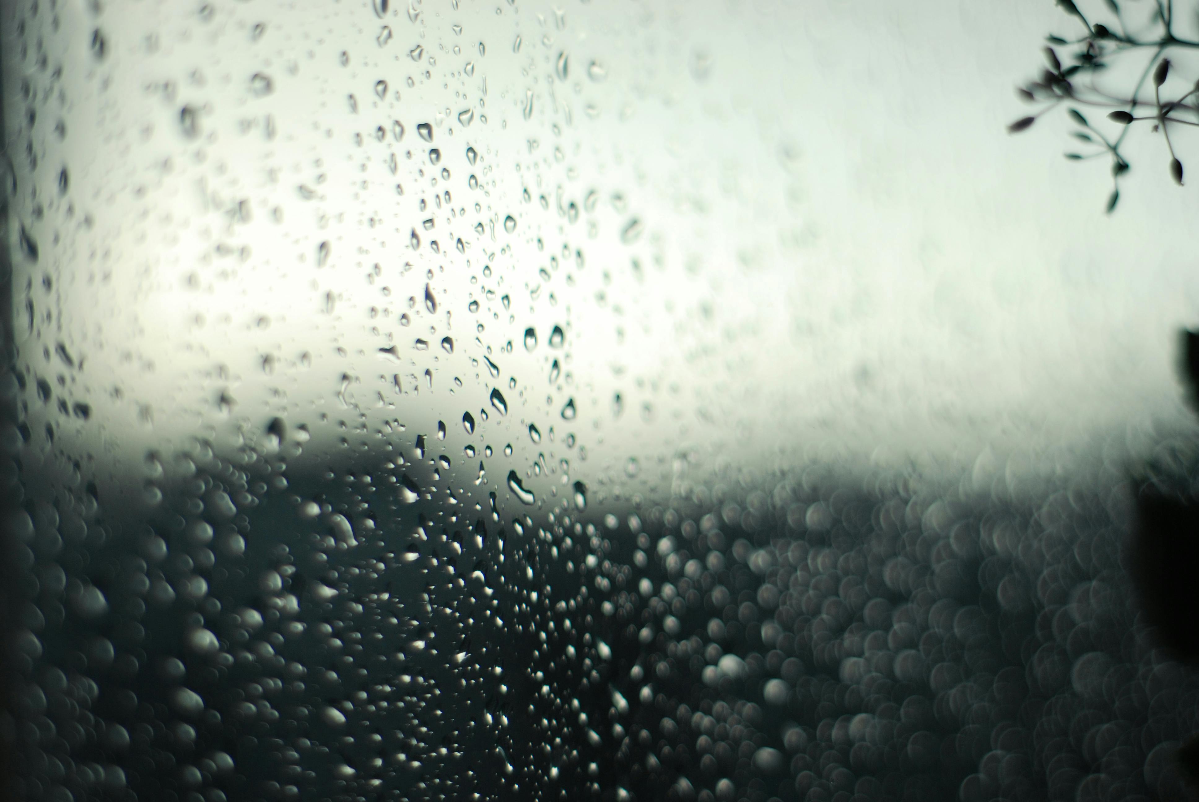 A dreamy view of raindrops on a window with a blurred natural backdrop, evoking tranquility.