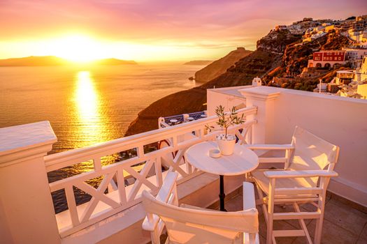 Idyllic Santorini sunset from a patio overlooking the caldera, with white chairs and table.