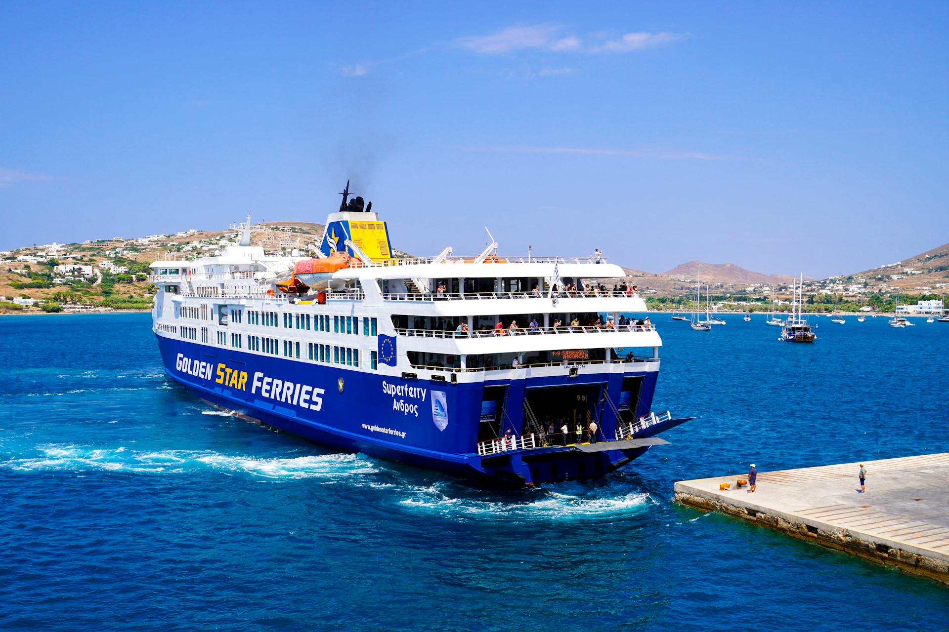 A vibrant image of a Golden Star ferry approaching a Greek island pier under a clear blue sky.