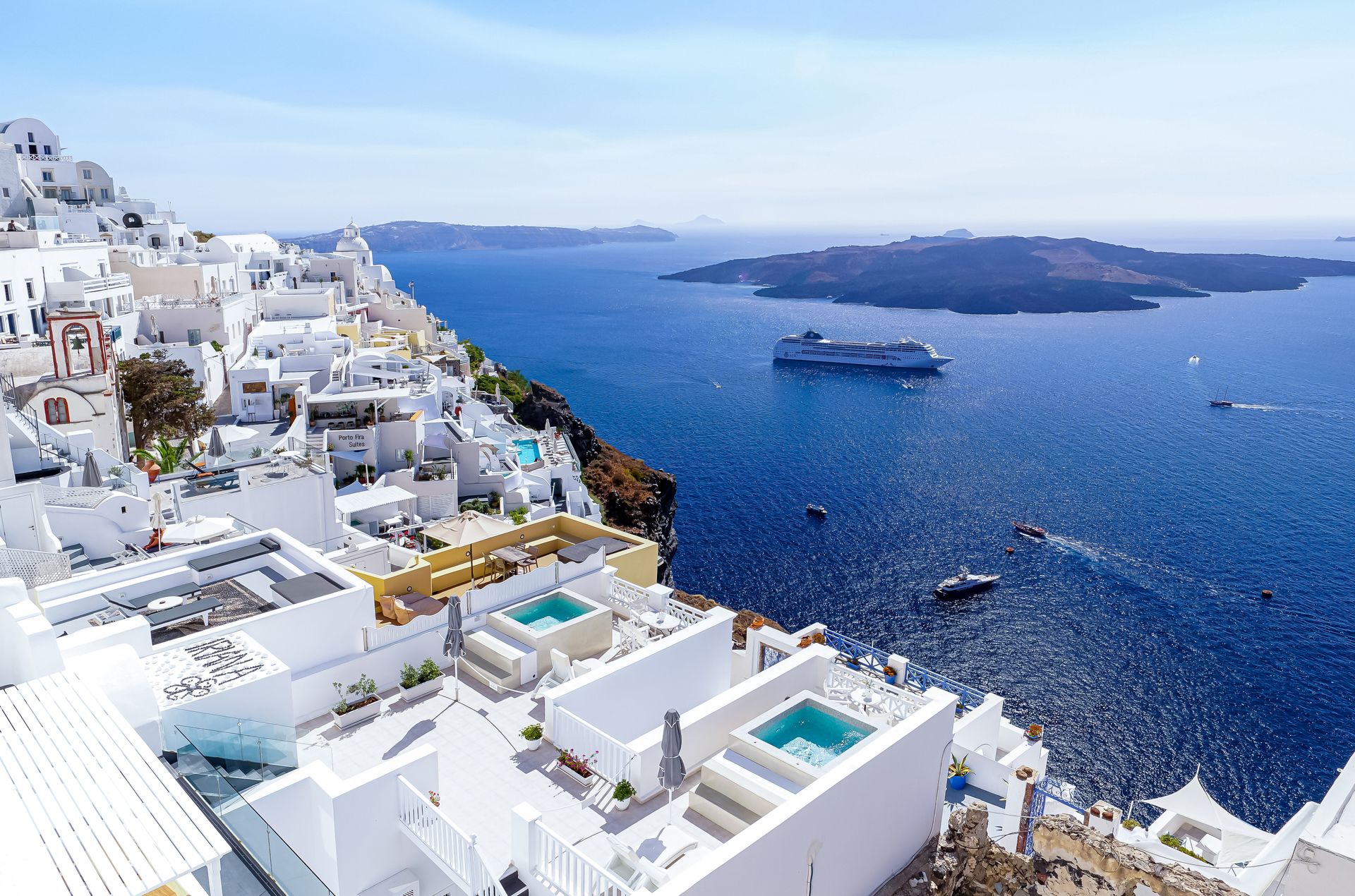 Breathtaking view of Santorini's white architecture and blue waters with cruise ships in the Aegean Sea.