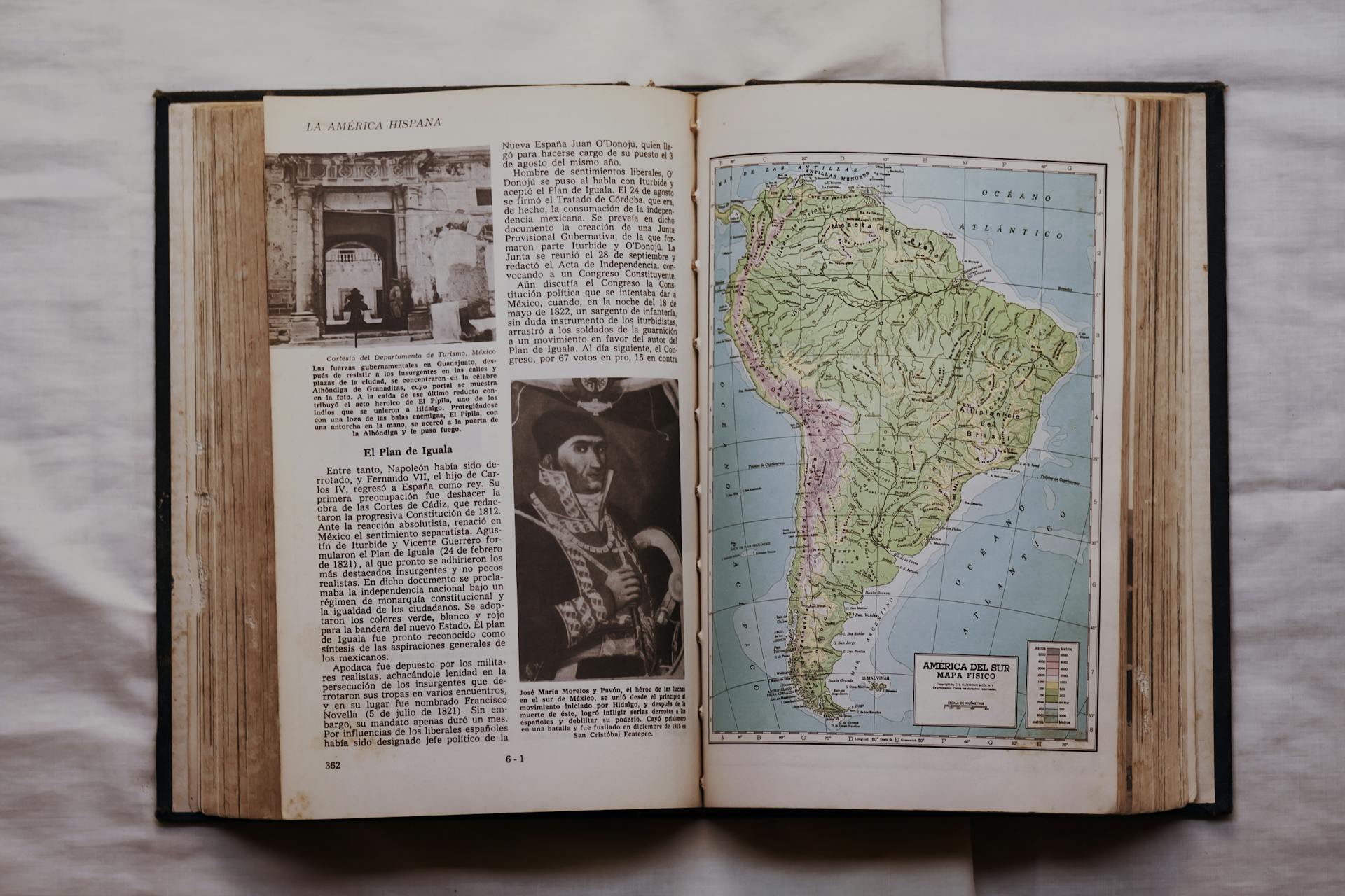 An open historical book displaying a map of South America and Spanish text, on a neutral background.