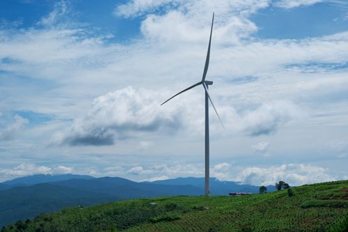 Free A scenic view of a wind turbine in a lush green countryside under a cloudy blue sky. Stock Photo