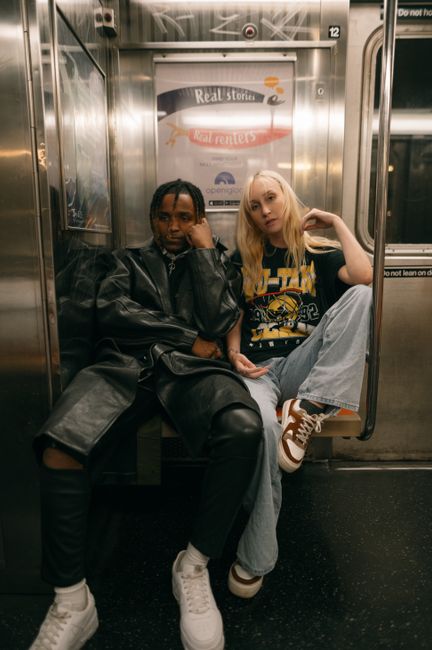 Stylish diverse couple posing in a subway train, showcasing urban fashion and attitude.