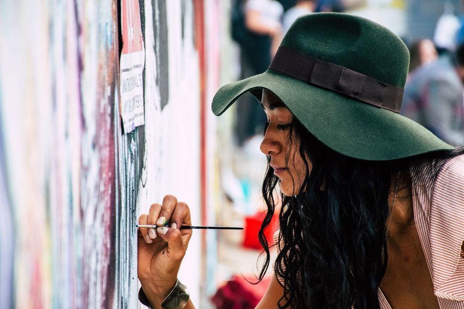 Woman artist painting a vibrant graffiti mural outdoors, expressing creativity.