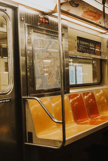 A vintage subway train interior with orange and yellow seats, handrails, and route map.