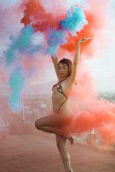 Model in bikini amidst colorful smoke outdoors, striking a pose with vibrant hues.