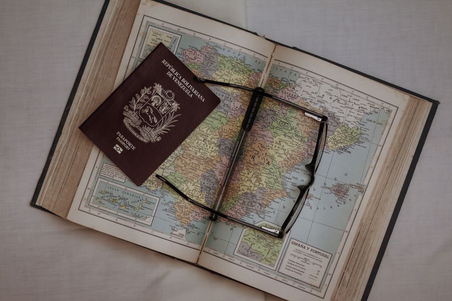 A Venezuelan passport and eyeglasses resting on an Atlas, showcasing travel and exploration.