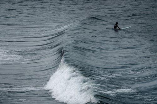 A Person Sitting on Surfboard Near Sea Waves