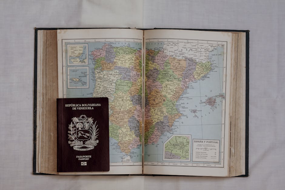 Open vintage atlas showing Spain and Portugal with a Venezuelan passport on top, symbolizing travel.