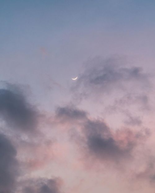 Free Crescent moon peeking through soft, colorful clouds at twilight, creating a serene and dreamy sky scene. Stock Photo