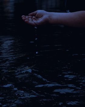 A hand dripping water into a river, capturing the essence of tranquility and nature.