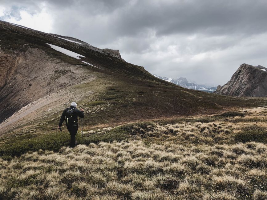 Person hiking in Turner Valley, AB, surrounded by rugged mountain landscape and dramatic skies.