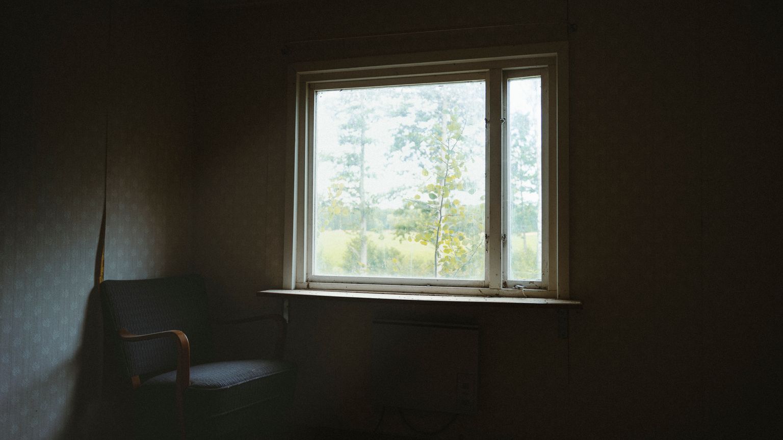 An empty chair beside a window in a quiet, dimly lit room