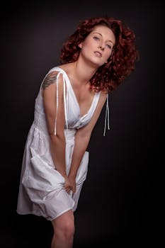 Elegant portrait of a woman in a white dress posing against a dark background.