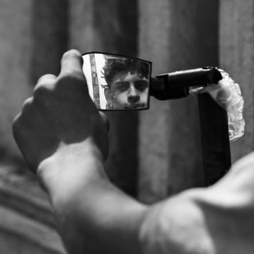 Grayscale Photo of Person Holding a Mirror