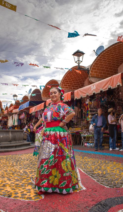 Free Woman in vibrant traditional Mexican dress posing in a lively outdoor market. Stock Photo