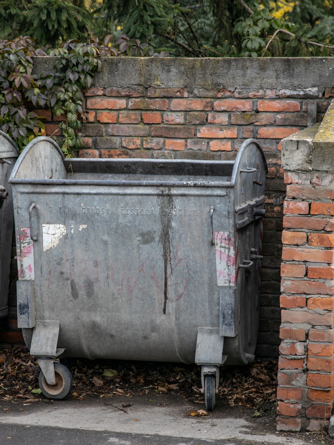 Large metal trash container positioned beside a brick wall outdoors