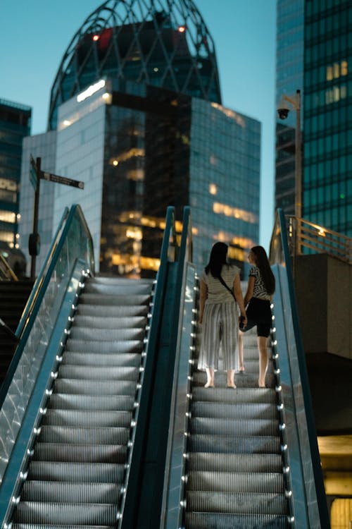 Two Women on Escalator Near Buildings