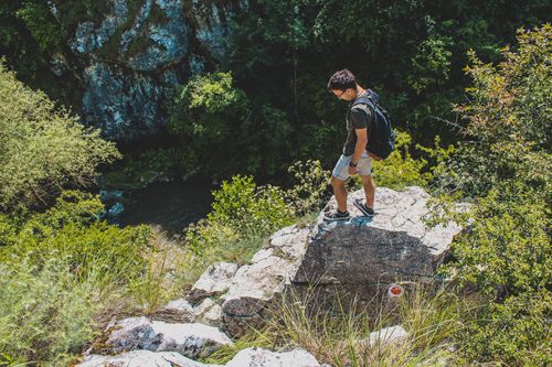 Free Man stands on cliff edge, enjoying a sunny day in nature. Stock Photo