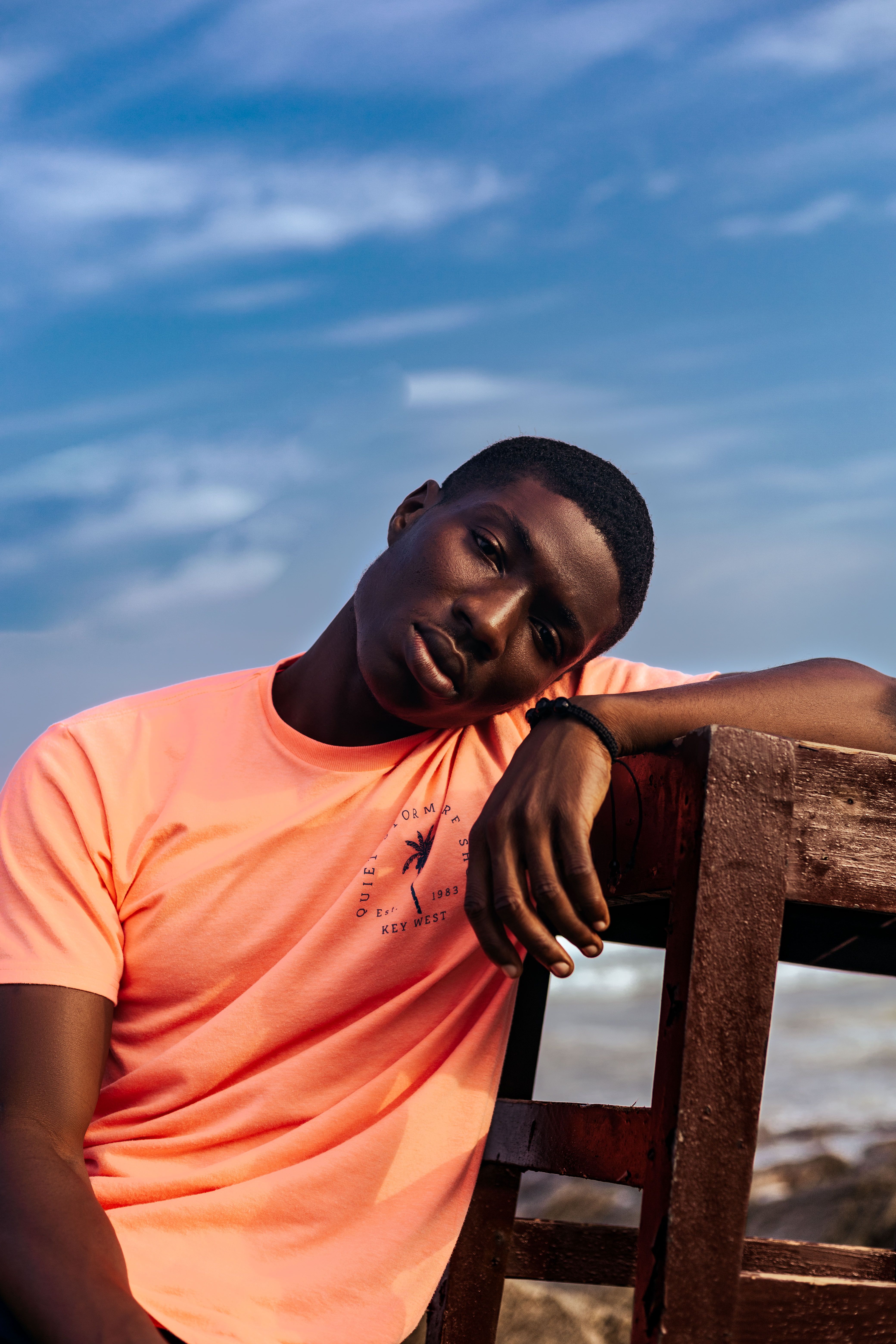 A man in a bright shirt poses by the ocean at Sakumono, Ghana, with a serene expression.