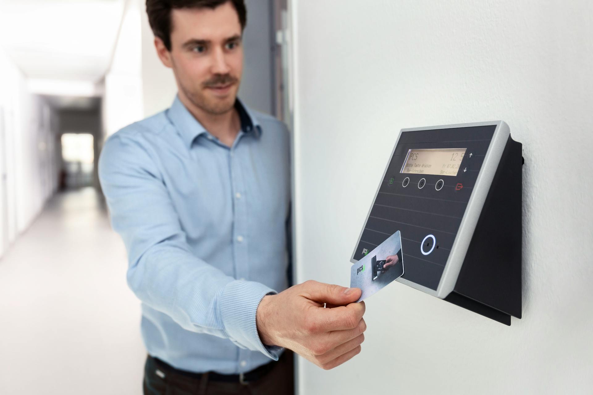 Professional man using access card on wall reader in office setting.