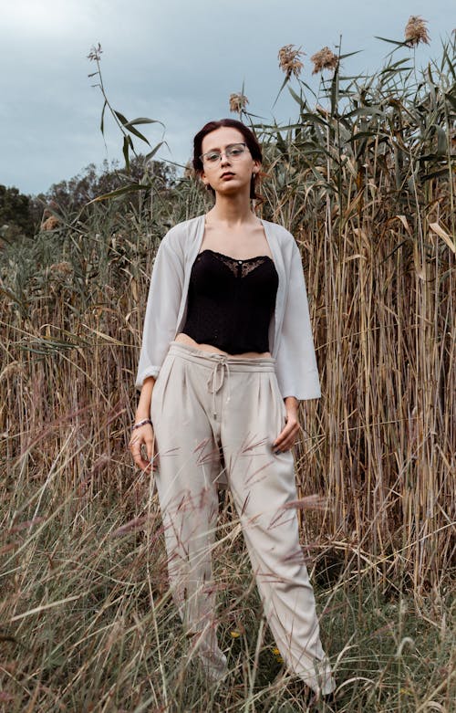 A Woman in Beige Pants Standing on Grass Field while Looking with a Serious Face