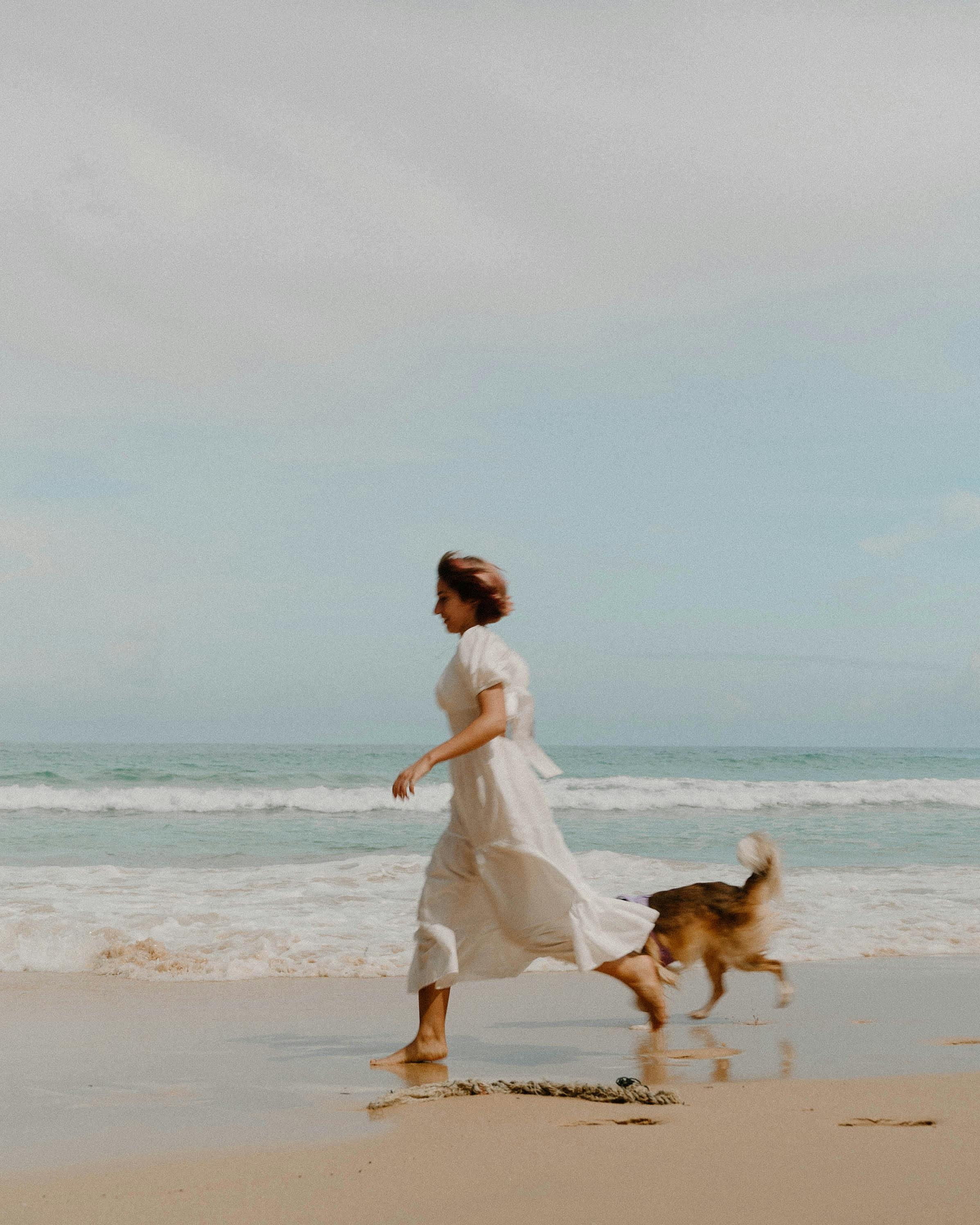 无忧无虑的女人和她的狗沿着泰国普吉岛的阳光海滩奔跑，拥抱夏日的快乐