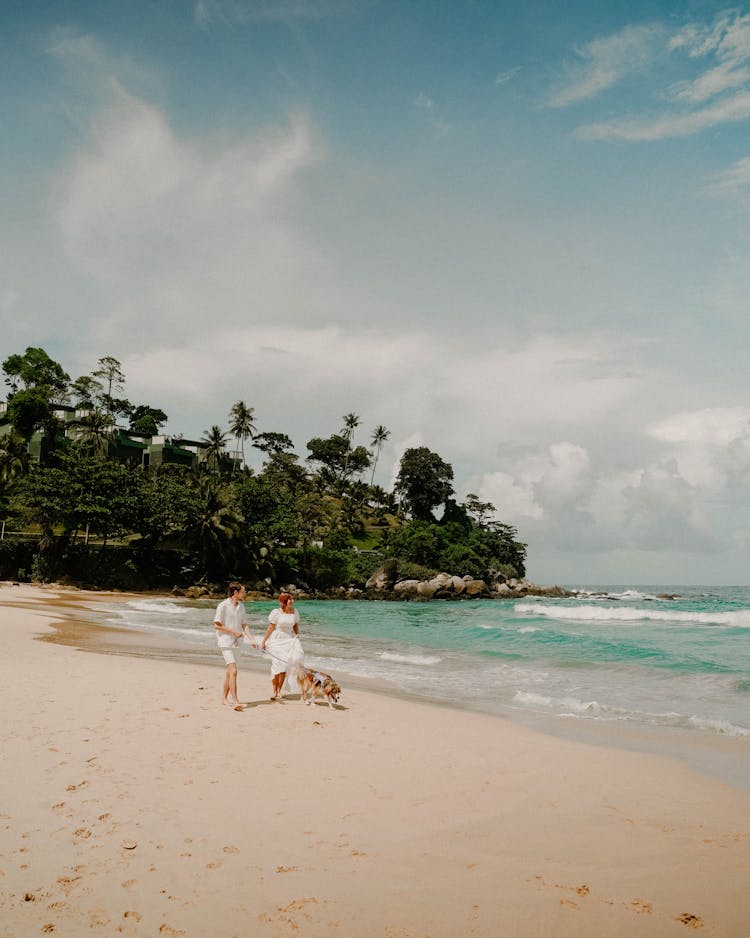 Man And Woman Walking Their Dog On The Beach 