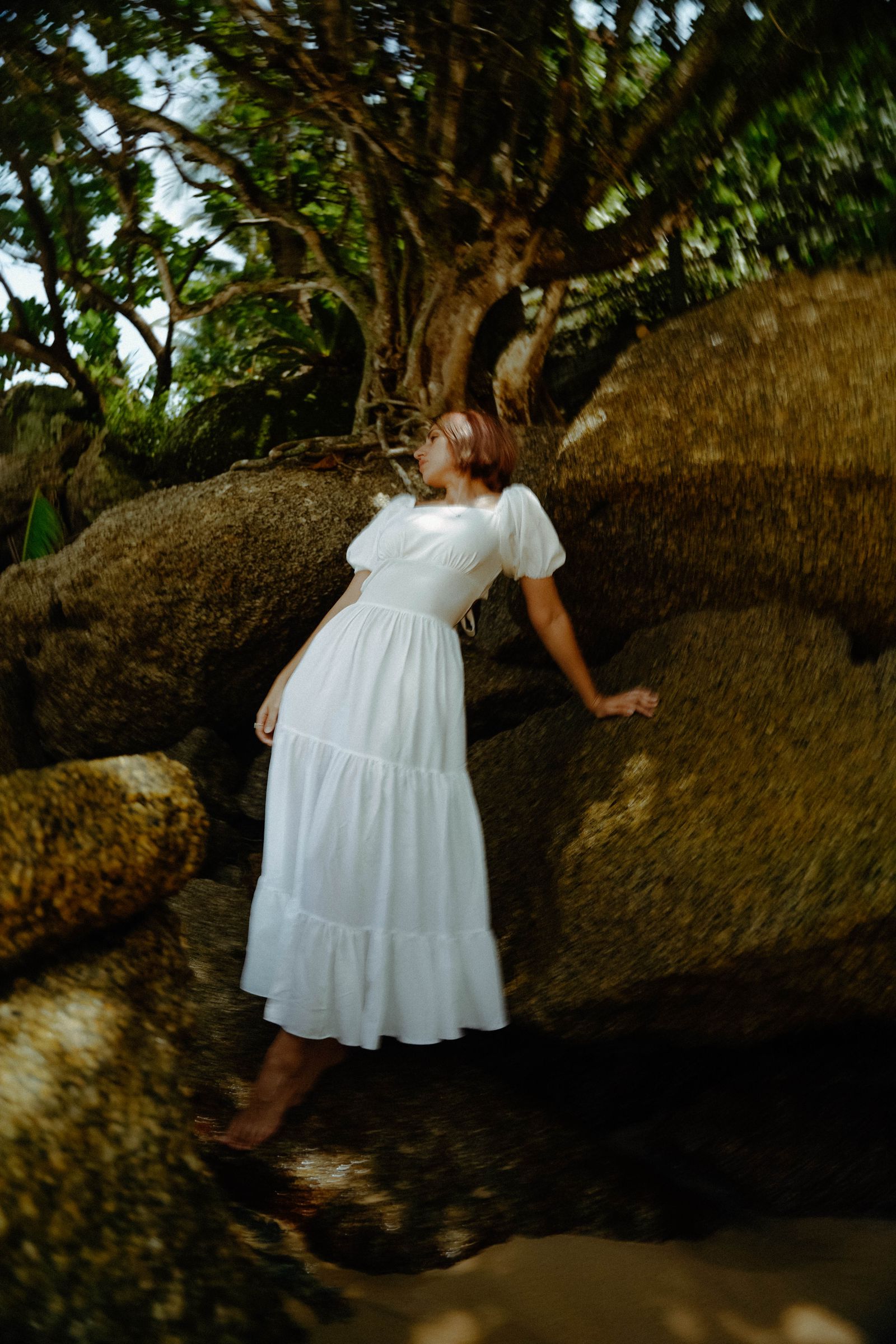 A woman in a long white dress standing between large rocks