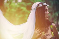 一位戴着花冠和面纱的新娘，优雅地站在郁郁葱葱的户外环境中，显得十分宁静