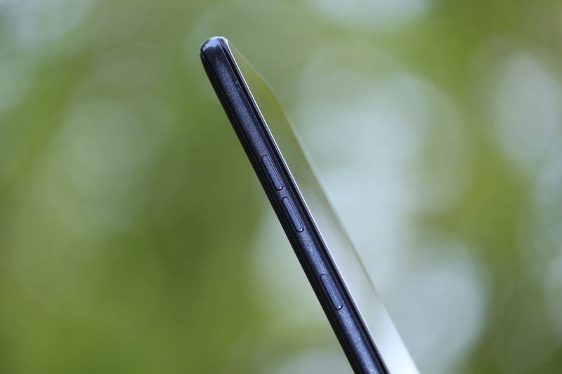 Detailed side view of a sleek smartphone with buttons, isolated on a green blurred background.