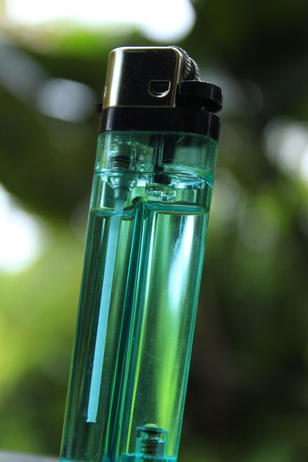 A detailed vertical shot of a transparent green lighter against a blurry background.